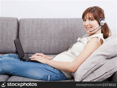 Beautiful young woman at home with a laptop and speaking over the internet with headphones
