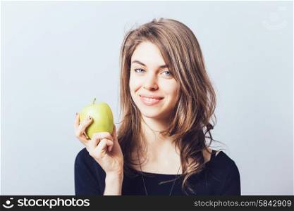 Beautiful young woman bites a green apple on a gray background