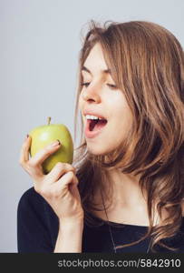 Beautiful young woman bites a green apple on a gray background