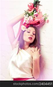 Beautiful young woman / bride in white dress holding bouquet of peonies lean against the wall