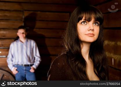 beautiful young woman brunette and young man in wooden log hut, woman standing near wall on background, focus on woman