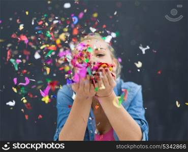 beautiful young woman celebrating new year and chrismas party while blowing confetti decorations to camera isolated over gray background