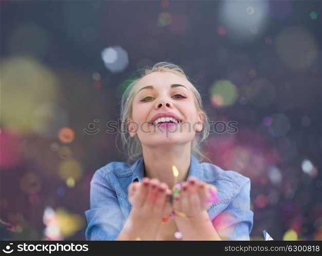beautiful young woman celebrating new year and chrismas party while blowing confetti decorations to camera isolated over gray background