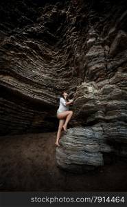 Beautiful young woman climbing up the high cliff on sea shore
