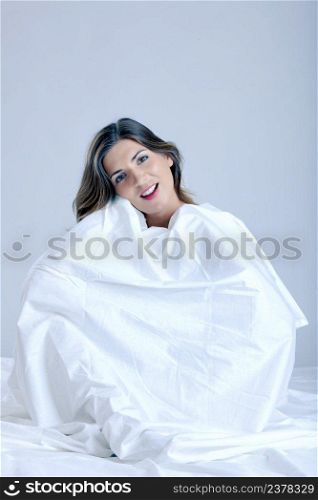 Beautiful young woman covered with white sheets on bed