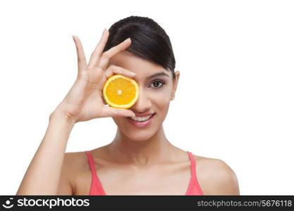 Beautiful young woman covering her eyesight from a slice of orange