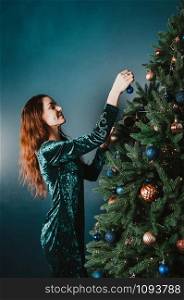 Beautiful young woman decorating Christmas tree, smiling. New Year concept. Home and family warmth. Luxury green, blue, golden colors. Banner for holiday theme