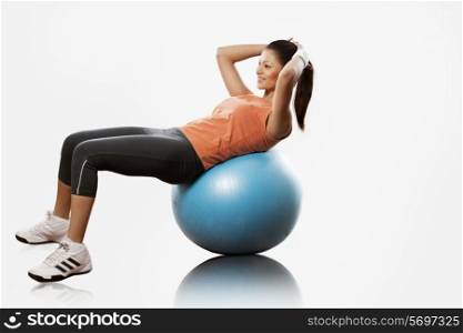 Beautiful young woman doing abdominal exercise on a fitness ball over white background