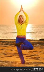 Beautiful young woman doing fitness exercise on a beach at sunset