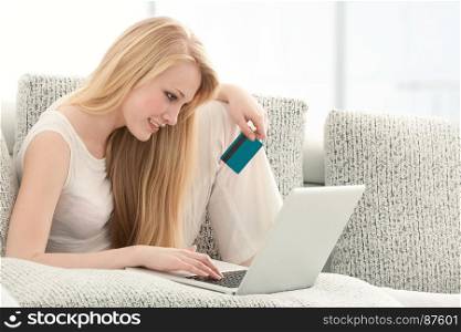 Beautiful Young Woman Doing Online Shopping on Laptop with a Credit Card, Sitting on the Sofa in Living Room