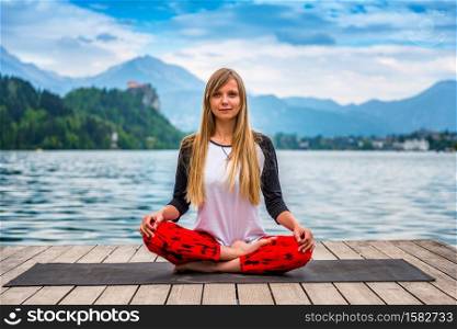 Beautiful young woman doing yoga by the lake