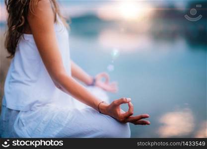 Beautiful young woman doing yoga exercise by the lake. Sitting in lotus position