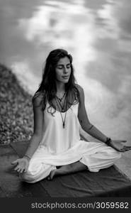 Beautiful young woman doing yoga exercise by the lake. Sitting in lotus position