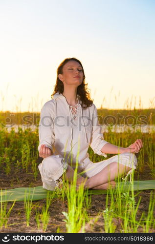 Beautiful young woman doing yoga sitting near the lake early in the morning