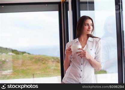 beautiful young woman drink first morning coffee at modern home interior with rain drops on big window door glass