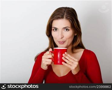 Beautiful young woman drinking a hot cofee, against a gray wall