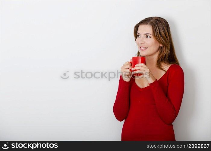 Beautiful young woman drinking a hot coffee, against a gray wall