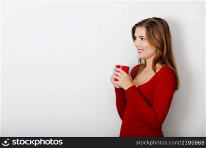 Beautiful young woman drinking a hot coffee, against a gray wall