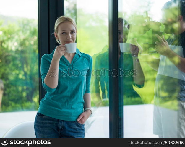 beautiful young woman drinking morning coffee by the window in her home