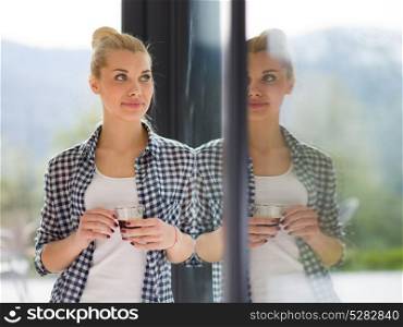 beautiful young woman drinking morning coffee by the window in her home