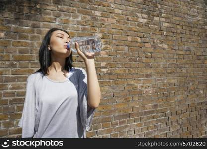 Beautiful young woman drinking water against brick wall