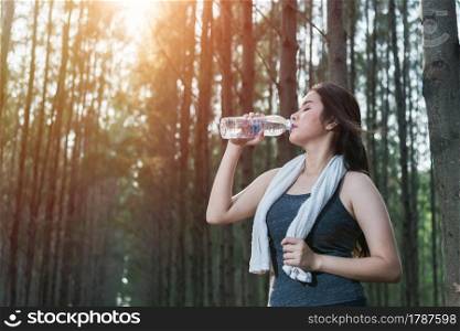 Beautiful young woman drinking water bottle after exercise fitness, in nature park forest