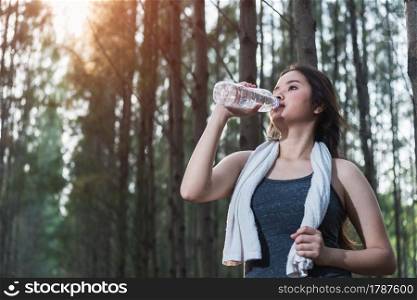 Beautiful young woman drinking water bottle after exercise fitness, in nature park forest