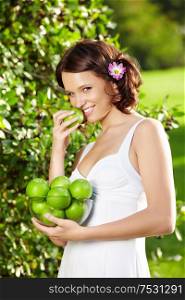 Beautiful young woman eats an apple in a summer garden