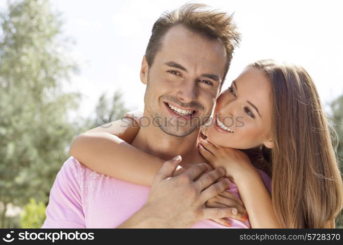 Beautiful young woman embracing man from behind in park