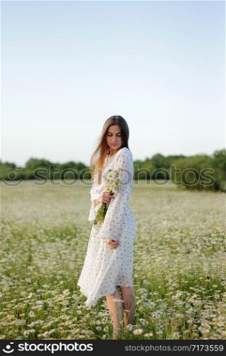 Beautiful young woman enjoying a field of daisies, beautiful girl relaxing outdoors, having fun, holding bouquet of daisies, happy young lady and spring-green nature, harmony concept. Beautiful young woman enjoying a field of daisies, beautiful girl relaxing outdoors, having fun, holding bouquet of daisies, happy young lady and spring-green nature, harmony concept.
