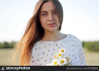 Beautiful young woman enjoying a field of daisies, beautiful girl relaxing outdoors, having fun, holding bouquet of daisies, happy young lady and spring-green nature, harmony concept. Beautiful young woman enjoying a field of daisies, beautiful girl relaxing outdoors, having fun, holding bouquet of daisies, happy young lady and spring-green nature, harmony concept.