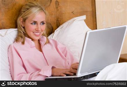 Beautiful young woman female teenager laying in bed wearing a pink short and using her laptop computer on the internet or on line for social media