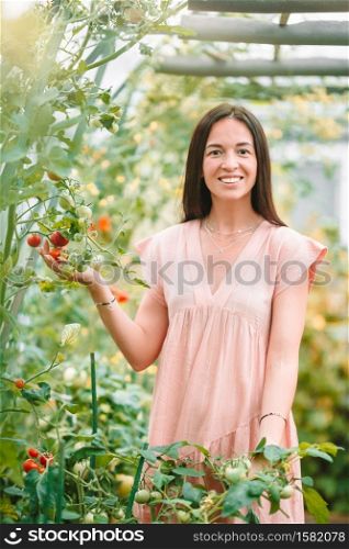 Beautiful young woman gardening in the greenhouse. Young woman holding a basket of greenery and onion in the greenhouse