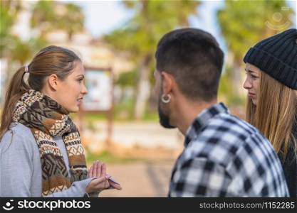 Beautiful young woman gestures while having an interesting discussion with two friends listening to her on an out of focus background. Friendship concept.. Young woman has a discussion with two of her friends