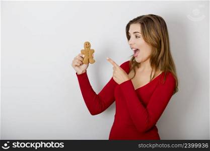 Beautiful young woman holding and pointing to a gingerbread cookie