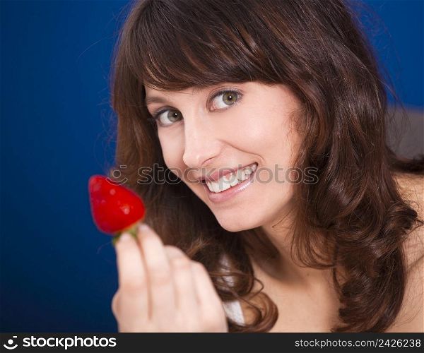 Beautiful young woman holding and showing a big and fresh strawberry