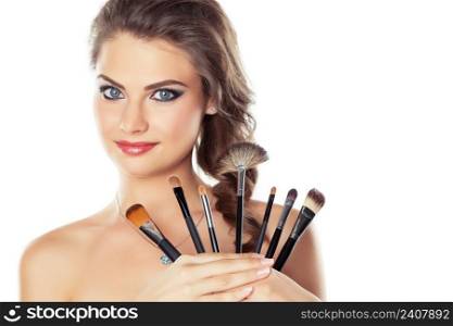 Beautiful young woman holding different make-up brushes, isolated on white