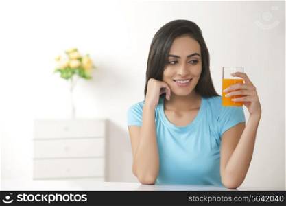 Beautiful young woman holding glass of fresh orange juice at home