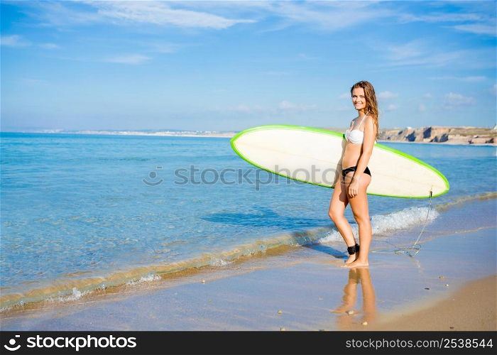 Beautiful young woman holding her surfboard and ready to surf