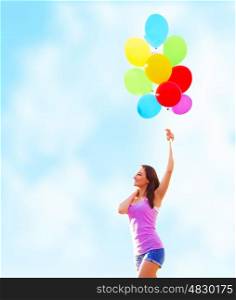 Beautiful young woman holding in hand many colorful balloons on blue sky background, summer time holiday, fun concept&#xA;
