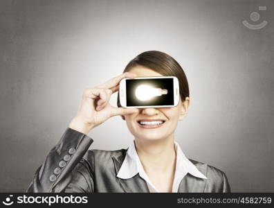 Beautiful young woman holding mobile phone against her eyes and smiling . Mobile phone demonstration