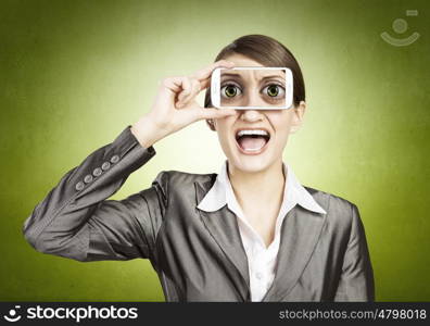 Beautiful young woman holding mobile phone against her eyes and smiling . Mobile phone demonstration