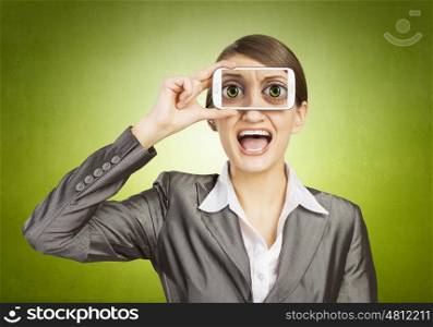 Beautiful young woman holding mobile phone against her eyes and smiling . Mobile phone demonstration