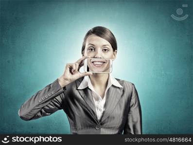 Beautiful young woman holding mobile phone against her mouth and smiling . Mobile phone demonstration