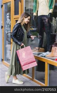 beautiful young woman holding shopping bag pointing finger window display