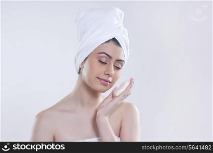 Beautiful young woman holding soap against gray background