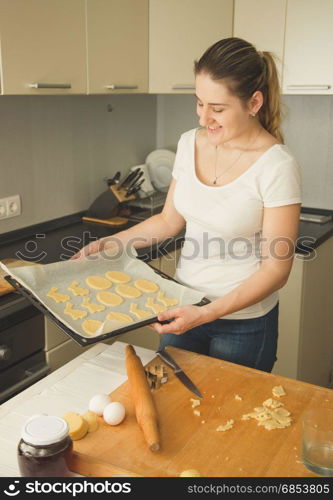 Beautiful young woman holding tray with raw cookies