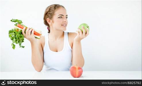 Beautiful young woman holding vegetables and fresh juice, sitting at a white table in light clothes on the light background