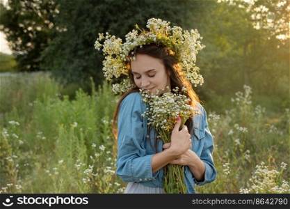Beautiful young woman holding wildflowers bouquet and  walking in flower field on sunset.