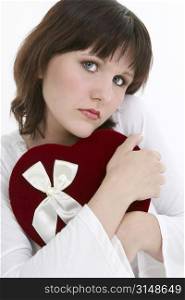 Beautiful young woman hugging a velvet heart shaped box of candy while looking dreamily into camera.